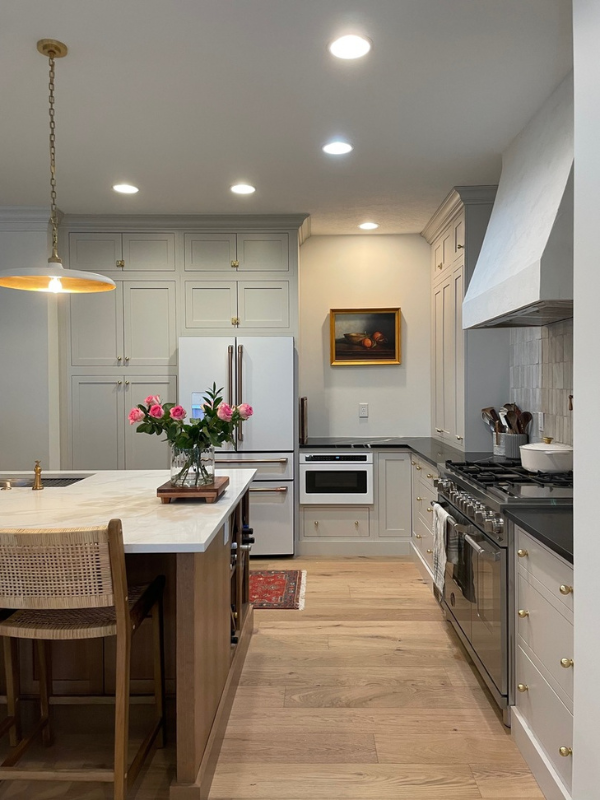 Cream colored inset shaker kitchen cabinets with warm wood-toned island, tan quartz countertops and textured glazed tile backsplash behind a tapered kitchen hood