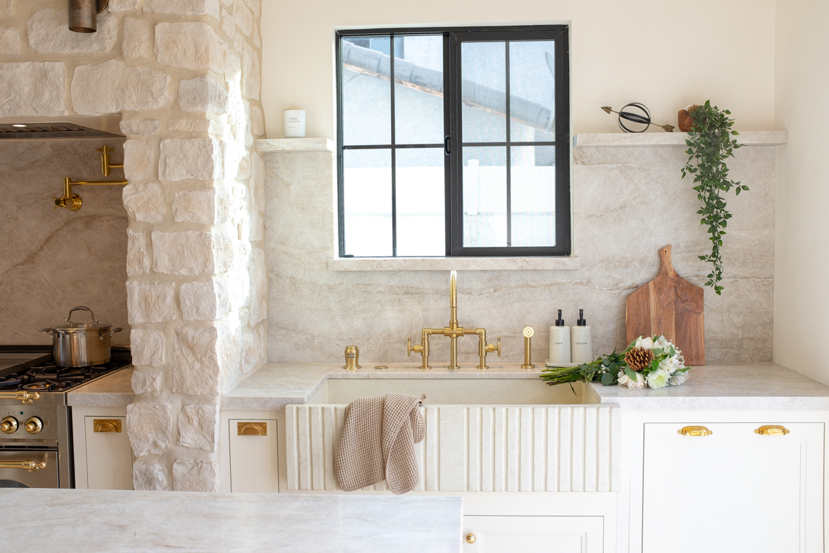 White inset base cabinets with a white fluted farmhouse sink and black-framed window above