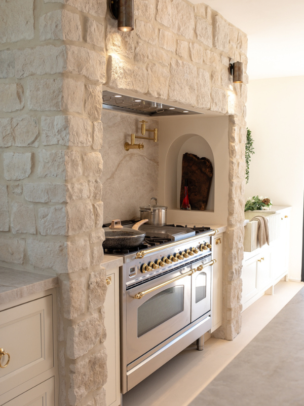 Mediterranean kitchen range wall with white inset base cabinets and a natural limestone range alcove