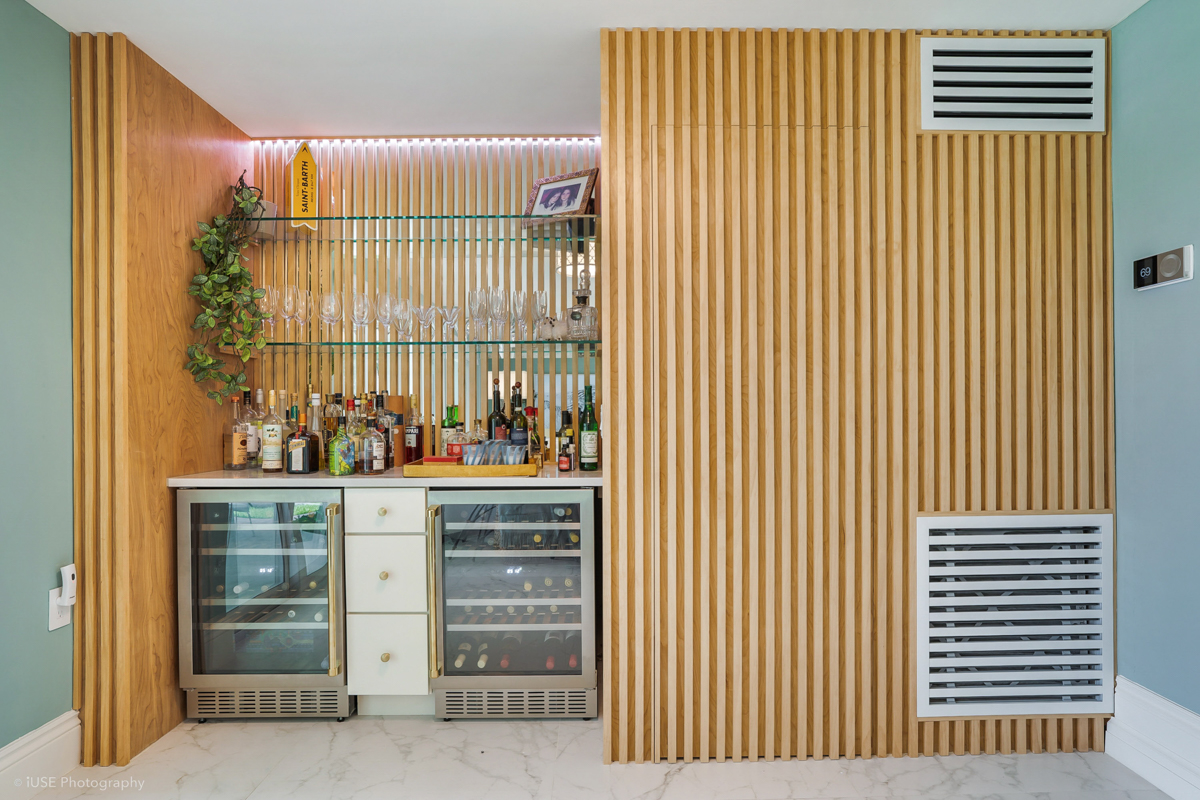 Built-in bar with two beverage coolers and a drawer base cabinet surrounded by vertical wood slat wall details