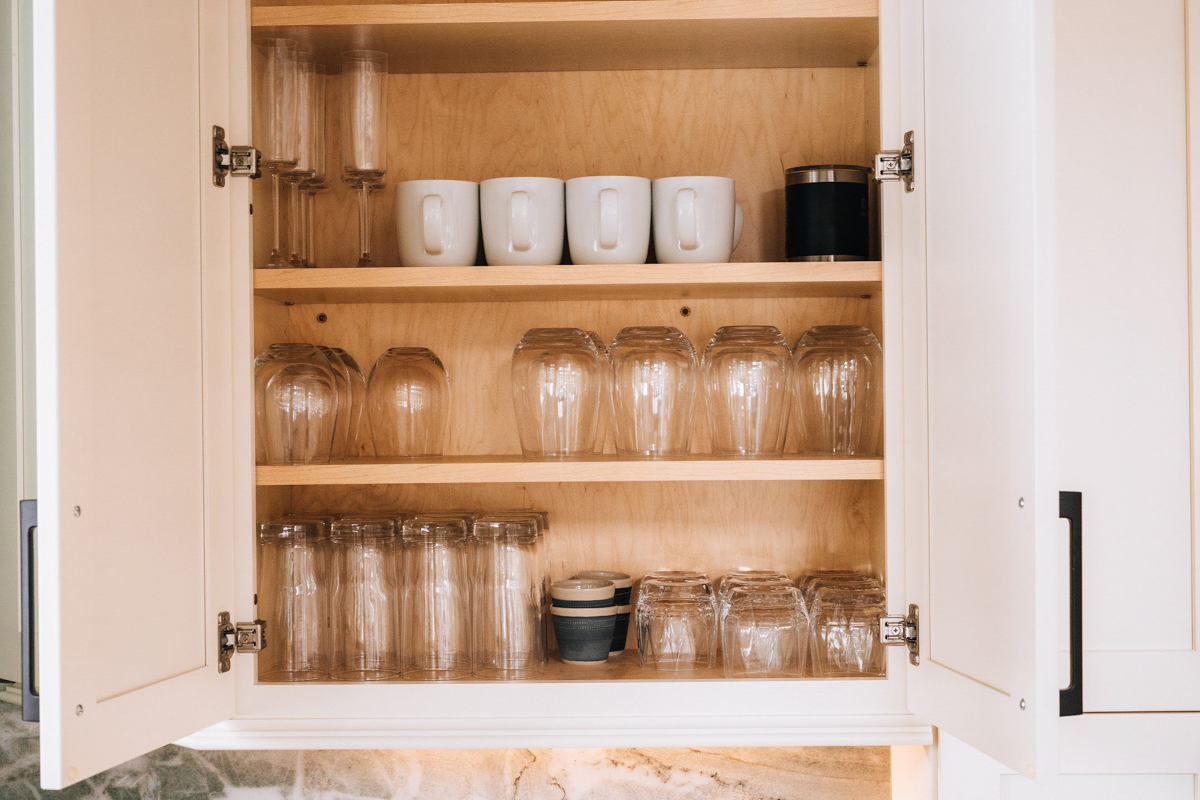 White shaker wall cabinet open displaying glassware and white coffee cups