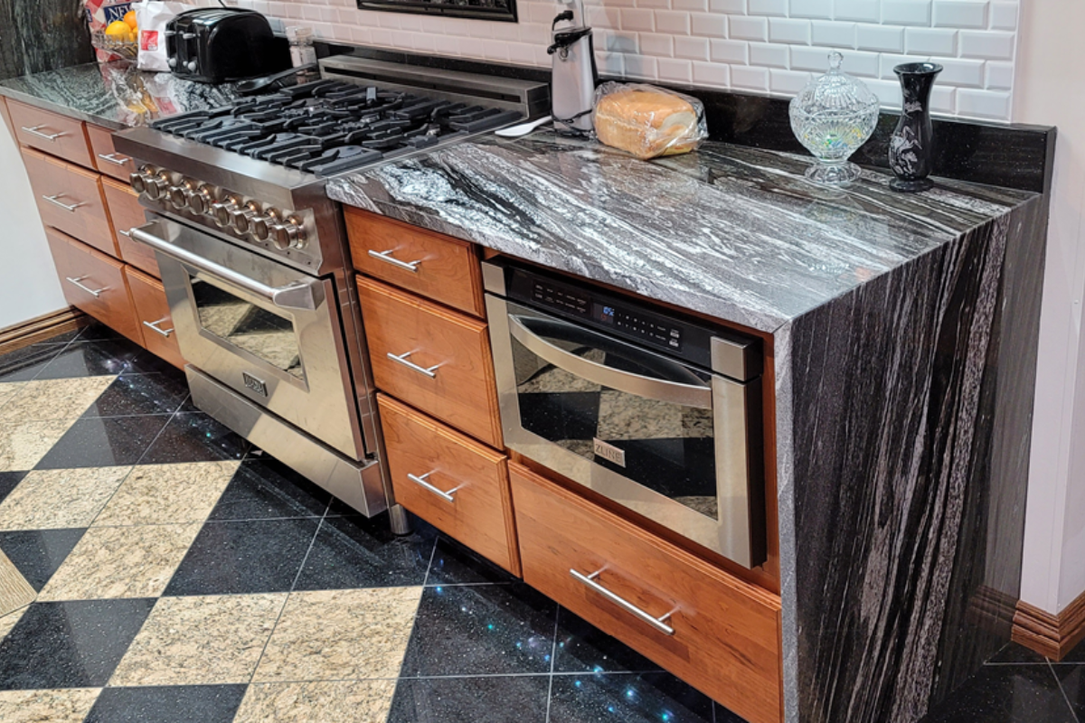 Raised panel cherry wood kitchen cabinets with black granite countertops and a waterfall edge