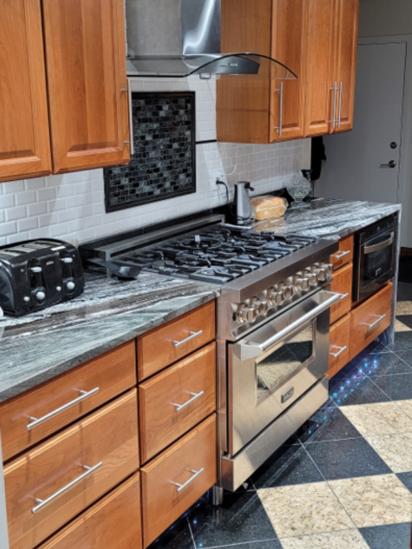 Raised panel cherry wood kitchen cabinets with black granite countertops and a waterfall edge