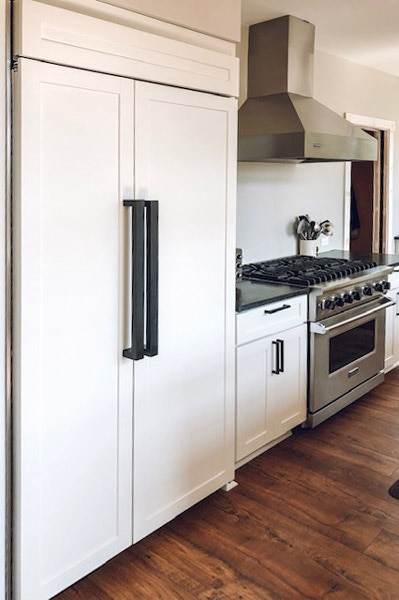 white Shaker cabinet front side-by-side refrigerator with large black door pulls next to stainless steel professional stove and range hood