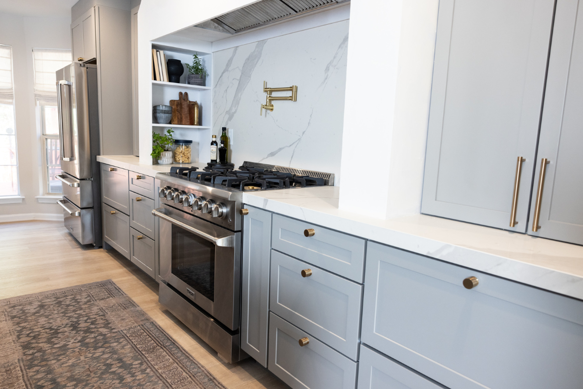 One-wall kitchen design with light gray shaker cabinets, a large white custom curved hood and white quartz countertops and backsplash