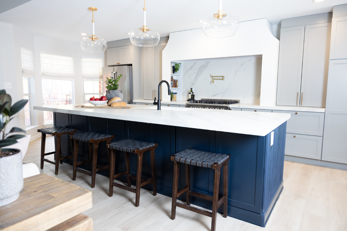 Large one-wall kitchen design with tall light gray shaker kitchen cabinets and gold cabinet hardware with a long dark blue kitchen island and white quartz countertops