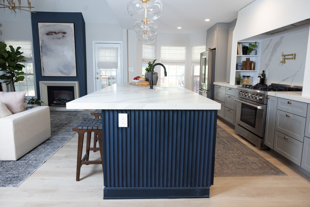 Large one-wall kitchen design with tall light gray shaker kitchen cabinets and gold cabinet hardware with a long dark blue kitchen island and white quartz countertops