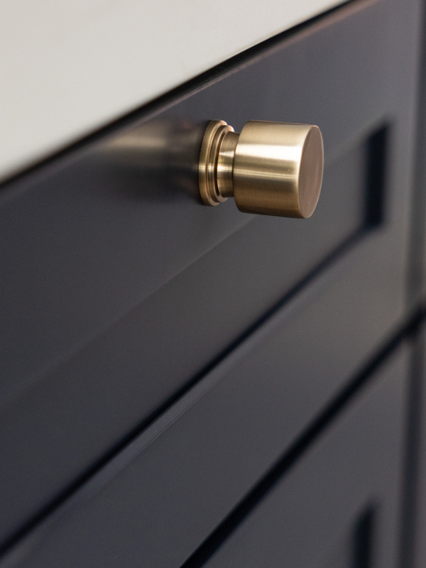 Close-up of dark blue shaker base cabinets with round golden knobs
