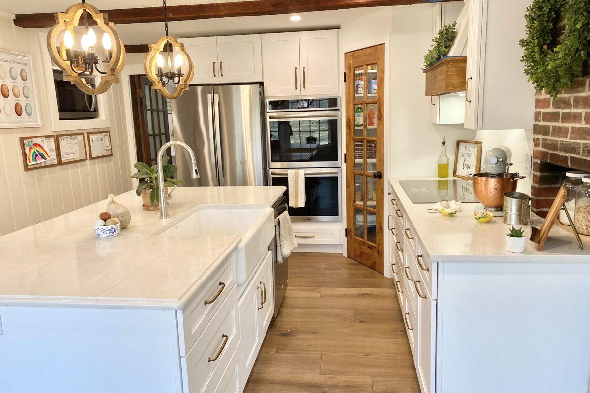 White shaker farmhouse kitchen with rustic wood beams, a large island, white quartz countertops and a large matching kitchen hood.