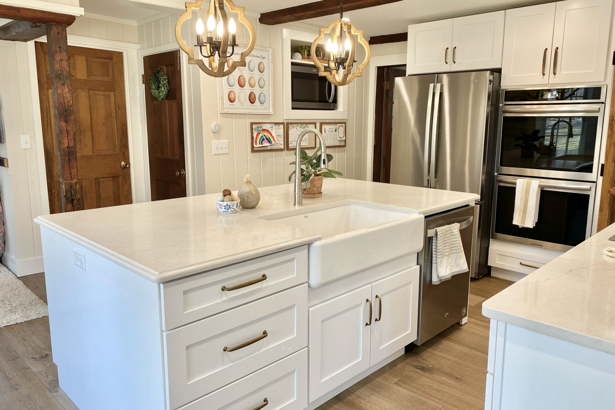 White shaker farmhouse kitchen with rustic wood beams, a large island, white quartz countertops and a large matching kitchen hood.