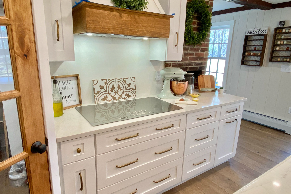 White shaker farmhouse kitchen with rustic wood beams, a large island, white quartz countertops and a large matching kitchen hood.