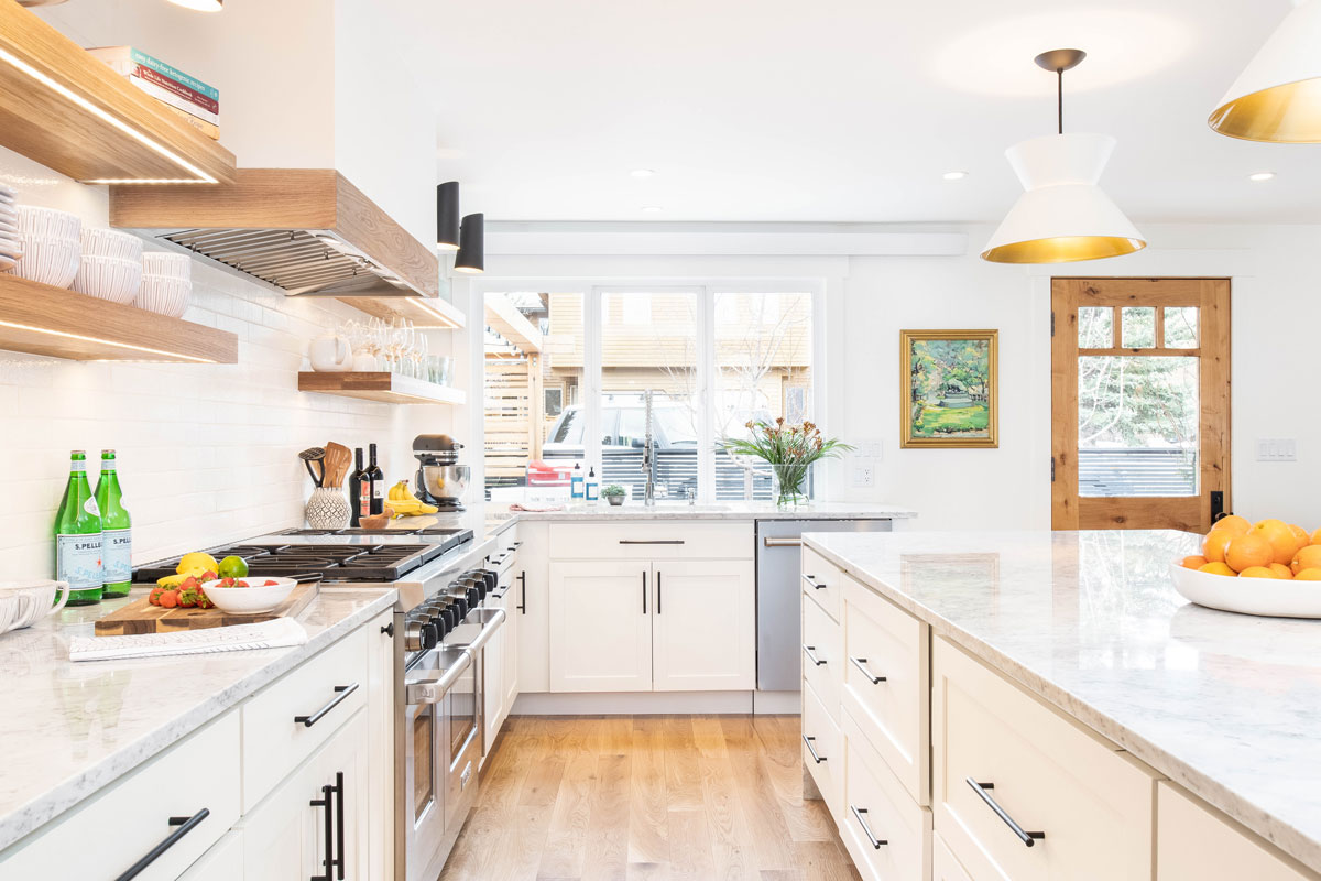 Painted White shaker kitchen base cabinets and island with white hood and natural wood floating shelves and large pendants