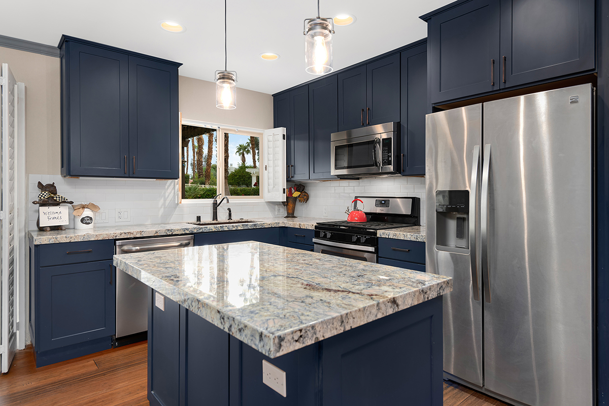 L-shaped blue painted shaker kitchen cabinets with island and gold, cream, and blue granite countertops