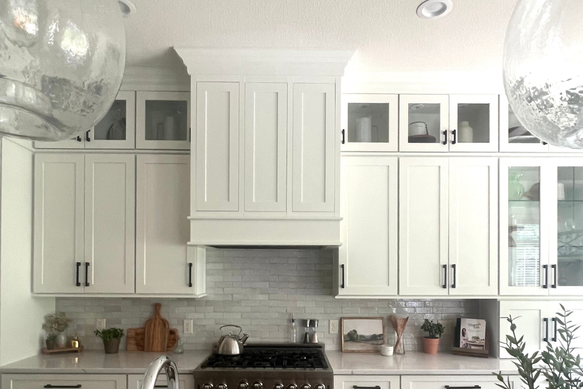 Close-up view of the custom shaker wood kitchen hood with stacked glass cabinets and glass pendant lights