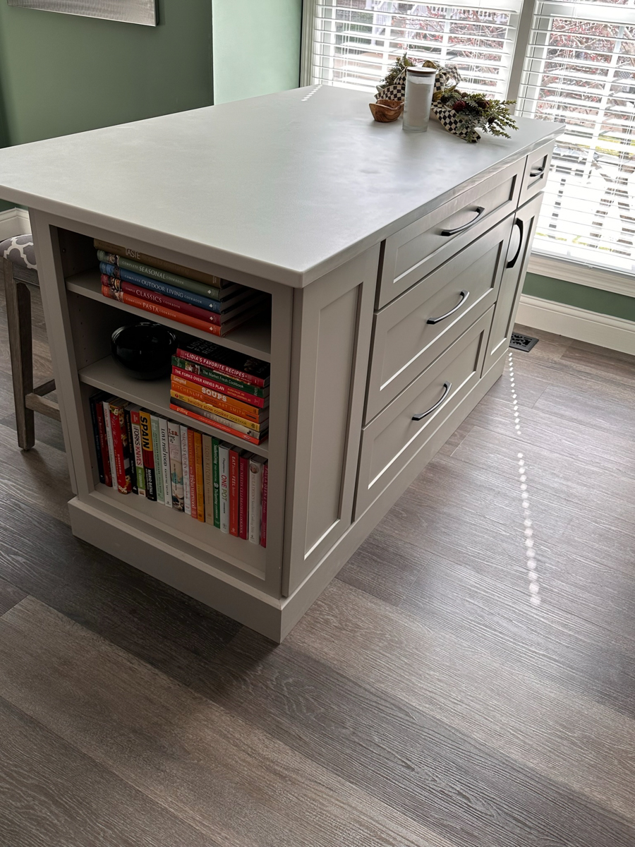 Light gray shaker kitchen cabinets with a small, decorative island with a built-in bookcase, green walls, and a neutral tile backsplash