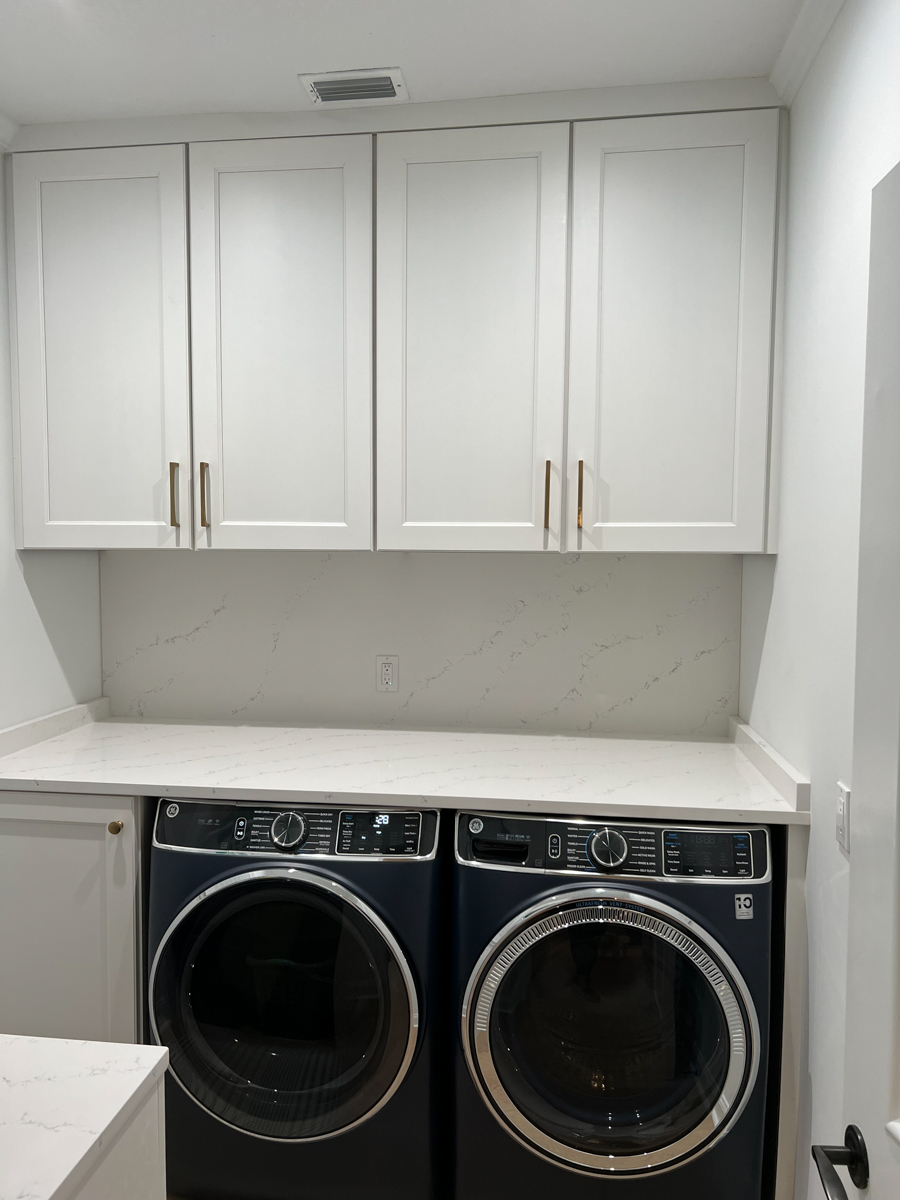 Decorative white shaker laundry room cabinets around a matching black front load washer and dryer.