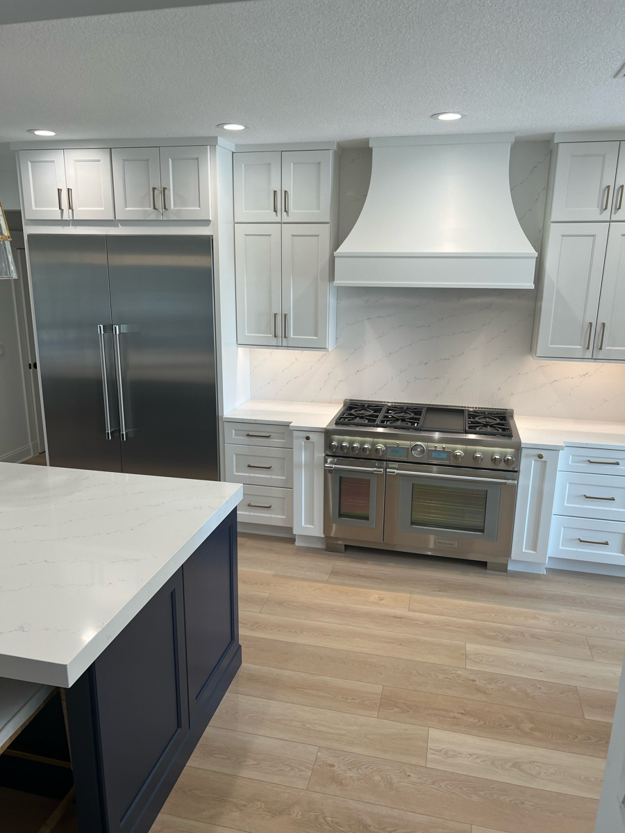 Grand decorative white shaker kitchen design with stacked cabinets, an artisan kitchen hood, navy blue island cabinets, and white quartz countertops