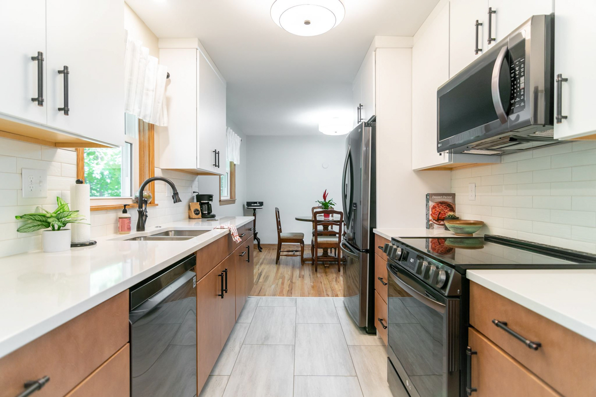 White slab kitchen wall cabinets with light brown slab base cabinets and black hardware