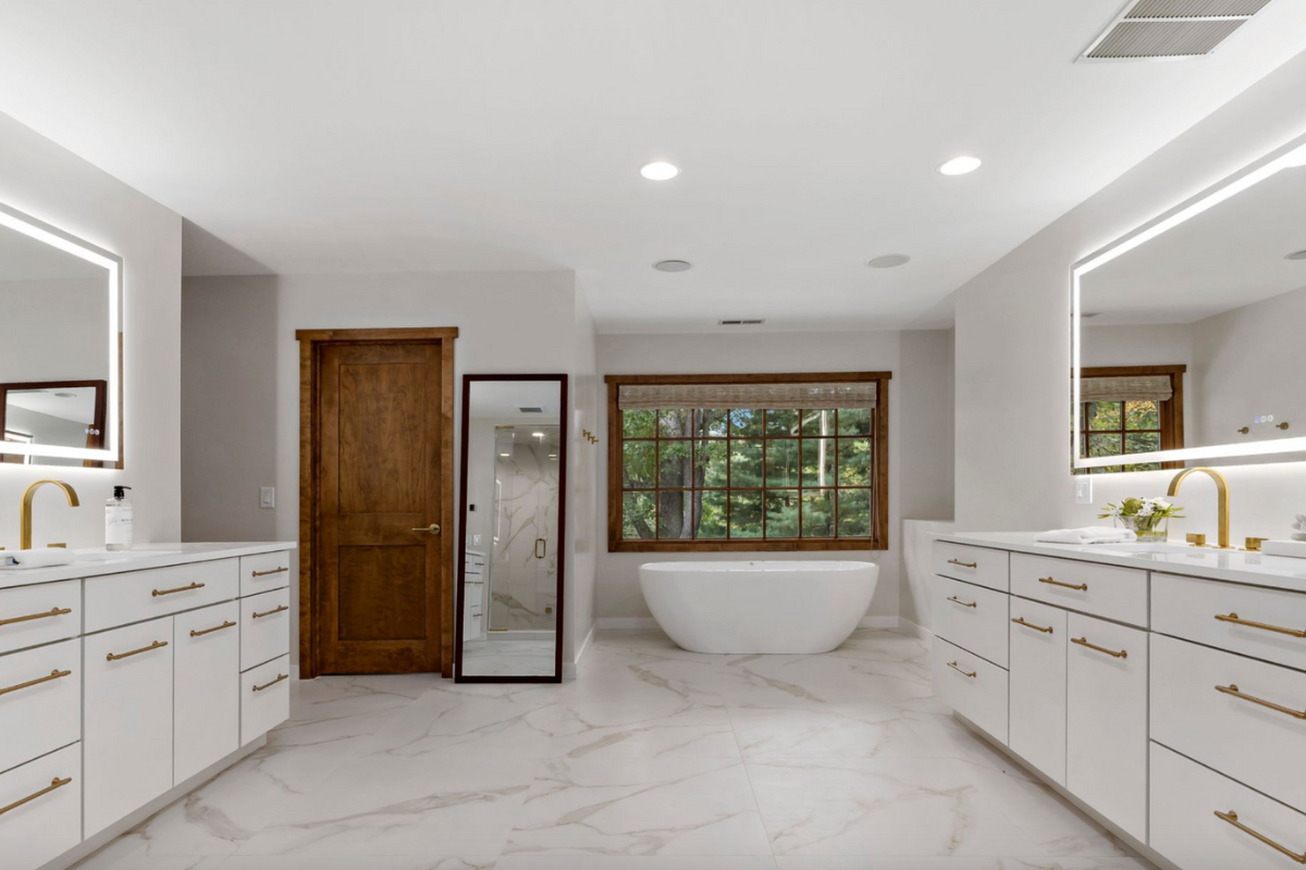 Two white slab master bathroom cabinets with white countertops and gold cabinet hardware