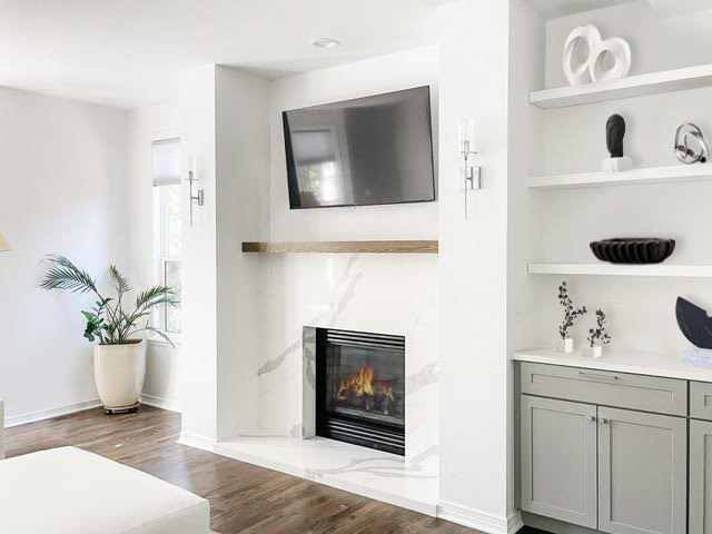 Light gray entertainment center cabinets with white floating shelves above and white quartz countertops