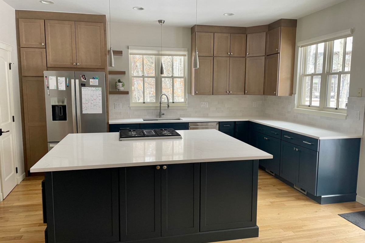 Light wood shaker kitchen wall cabinets with indigo shaker base and island cabinets with white quartz countertops