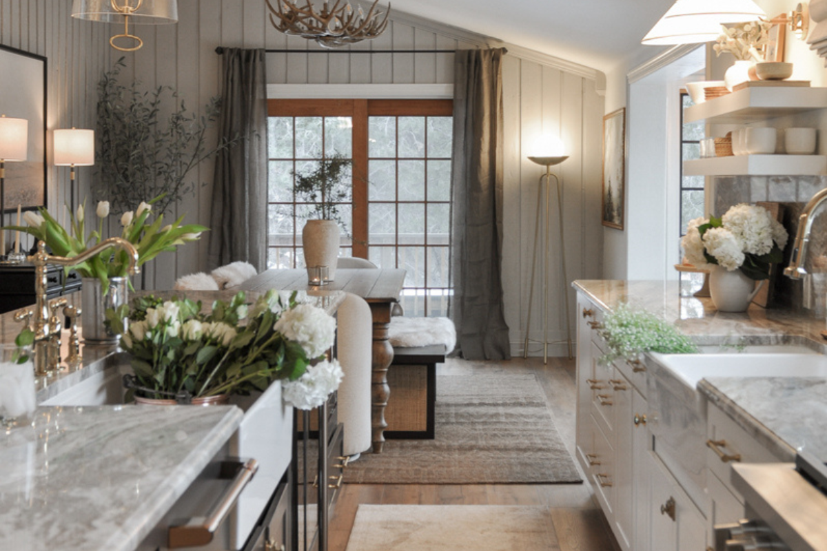 Luxe white stacked shaker kitchen cabinets, brass hardware, bronze metal kitchen hood, cream and brown marble countertops plus matching slab backsplash, and a large dark brown stained furniture-style island