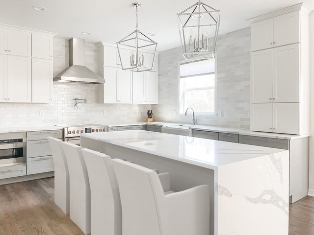 White and light gray shaker kitchen cabinets with white quartz waterfall countertops and polished chrome light fixtures