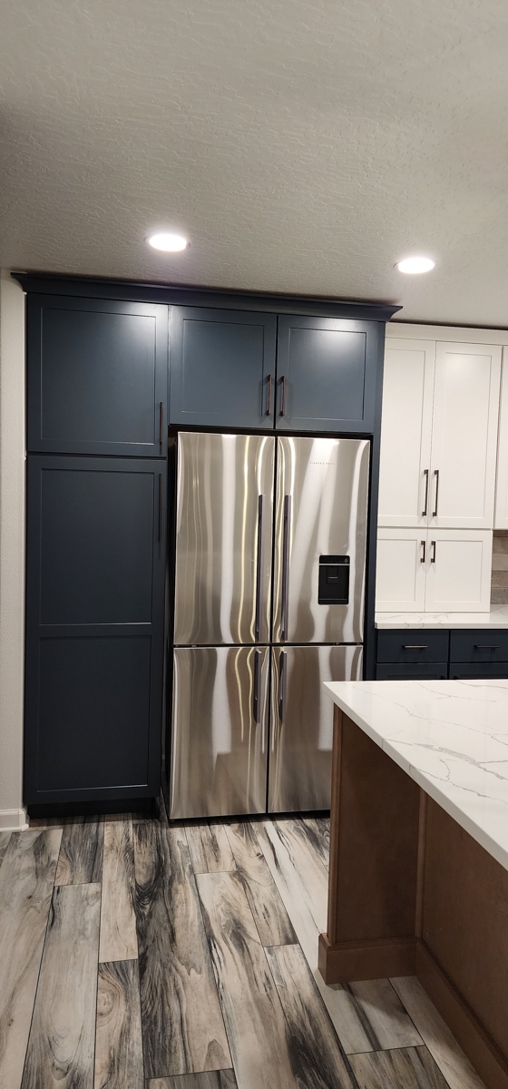 Farmhouse kitchen with white shaker wall cabinets, blue shaker base cabinets, and light wood furniture-style island