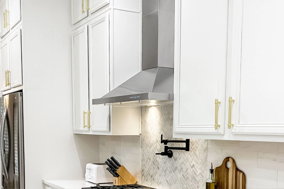 Wall-mount angled stainless steel range hood between white decorative cabinets