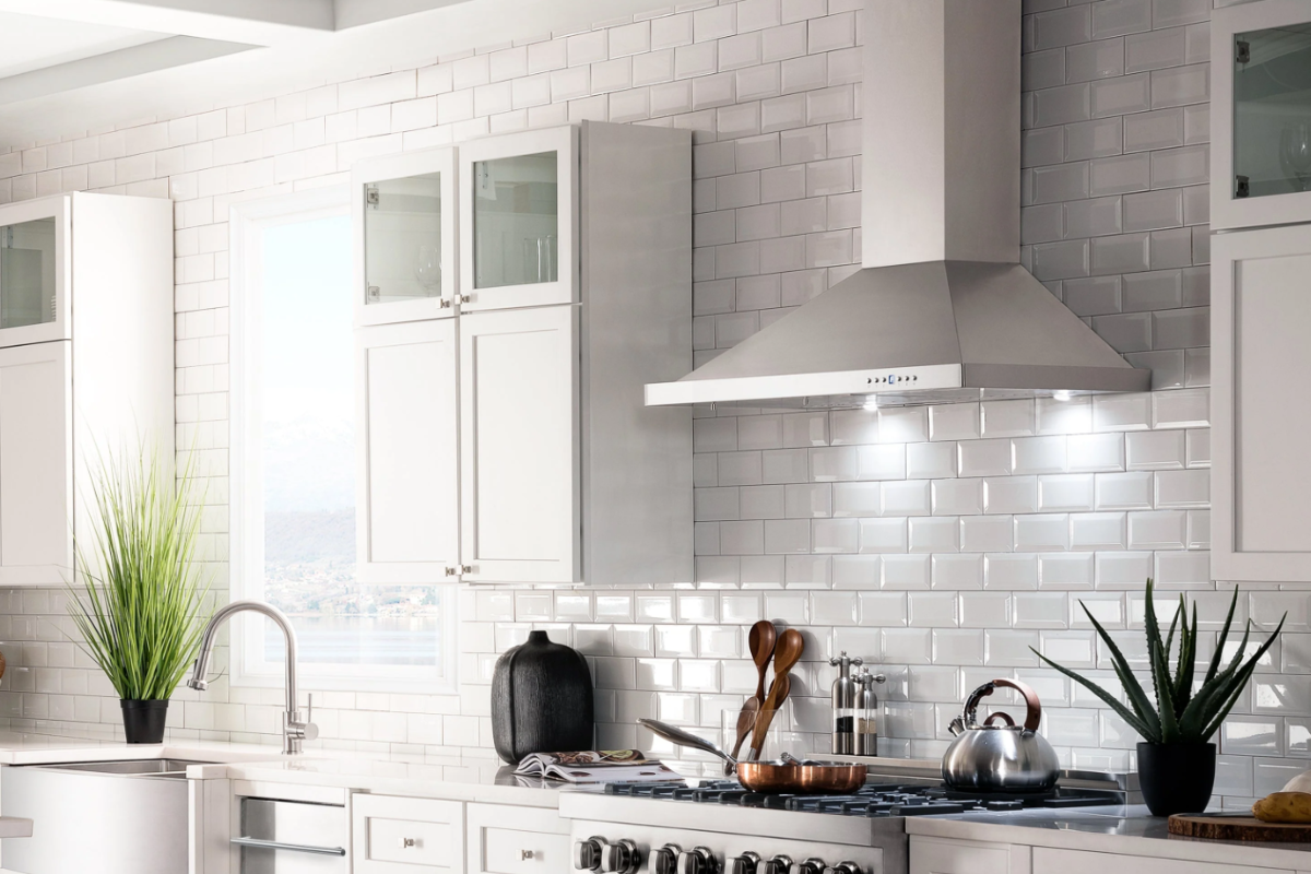 Angled stainless steel chimney hood between white stacked shaker kitchen cabinets