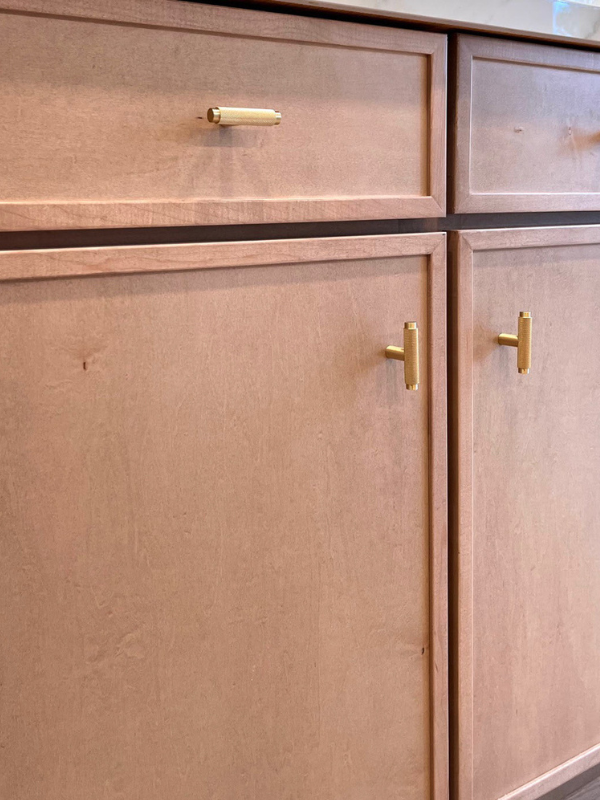 Close-up view of warm wood-tone thin shaker base cabinets with modern brass cabinet hardware