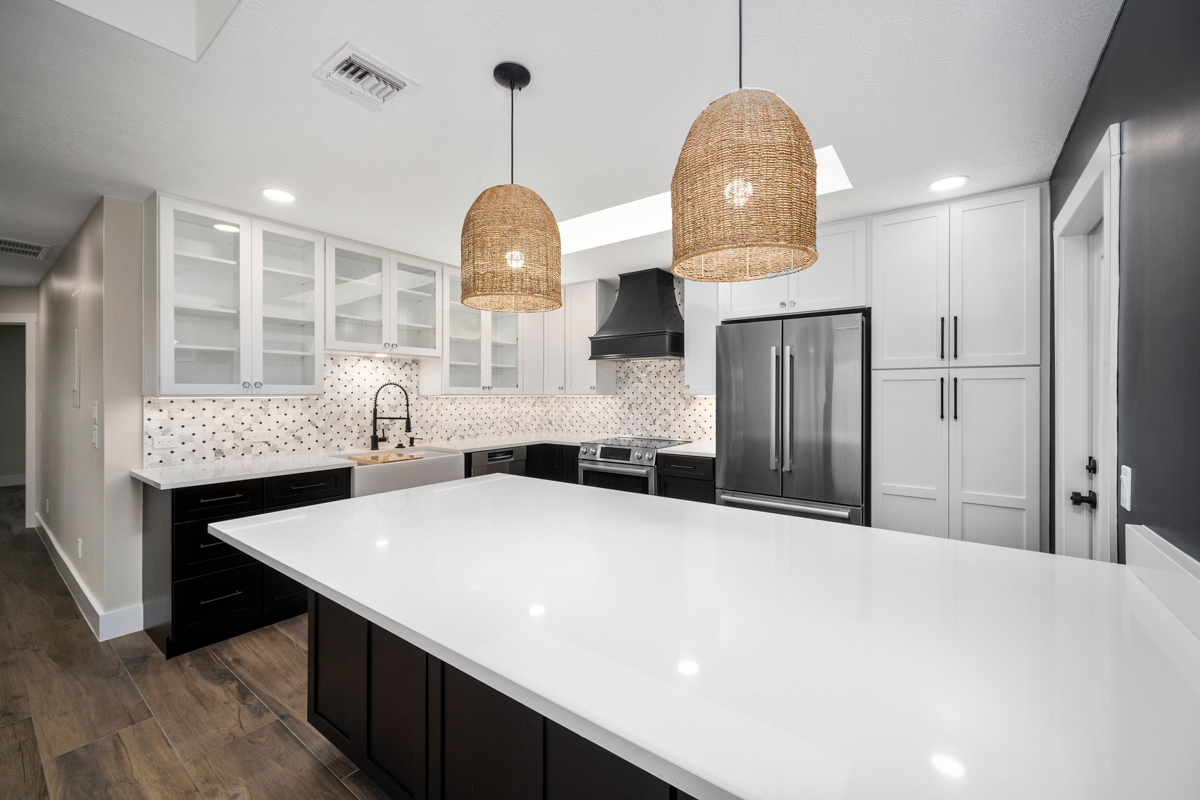 Bright kitchen with white wall cabinets with glass inserts and black base cabinets with white quartz countertops