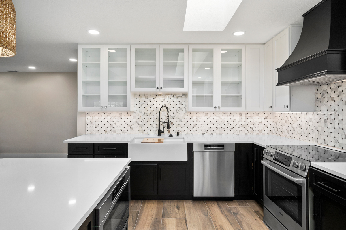 Bright kitchen with white wall cabinets with glass inserts and black base cabinets with white quartz countertops