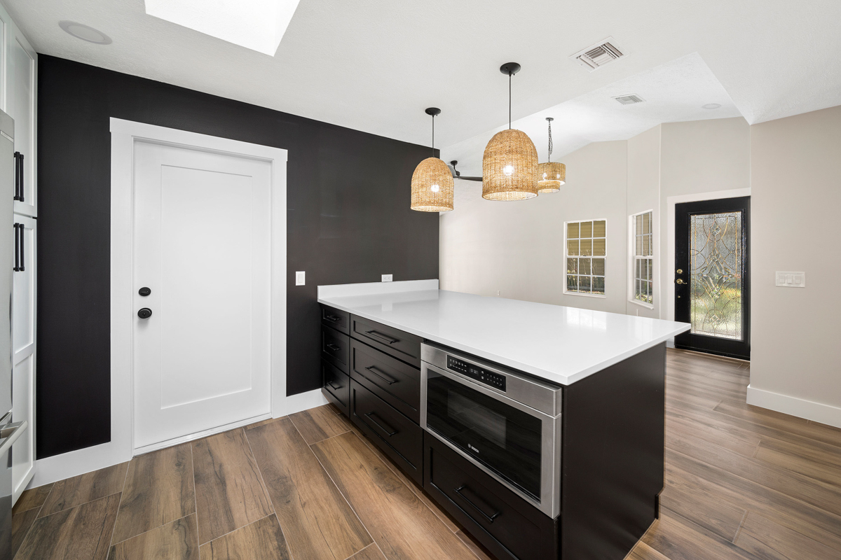 Bright kitchen with white wall cabinets with glass inserts and black base cabinets with white quartz countertops