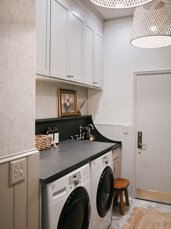 Left side of the laundry room with light taupe shaker wall cabinets above matching shiplap and black quartz countertops over a washer/dryer and sink