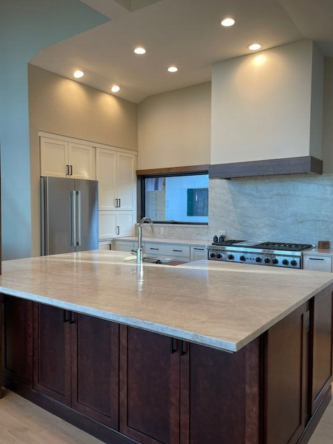 Large white shaker kitchen with a large dark brown wood island and creamy stone countertops