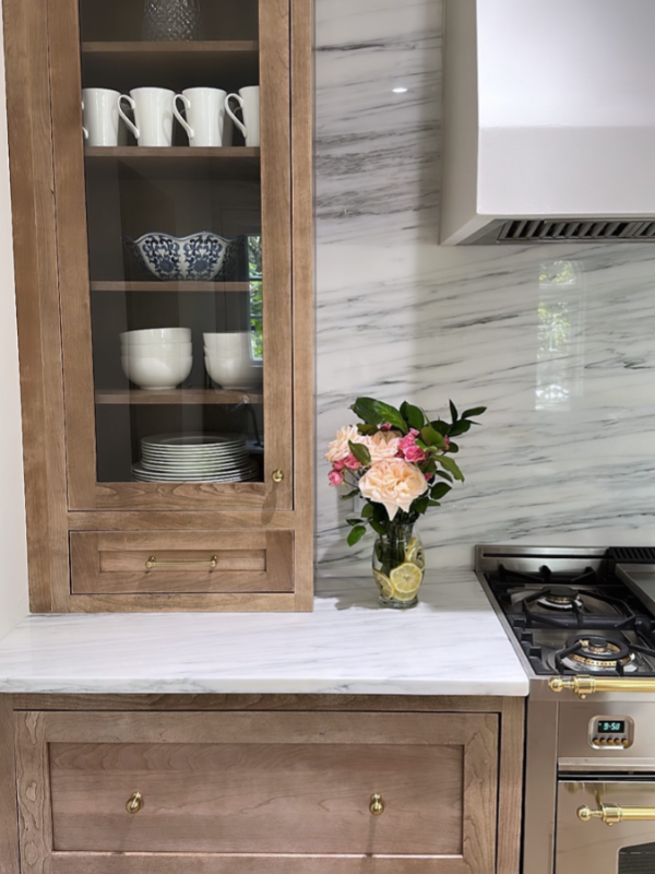 Close-up view of tall glass wall cabinets sitting on the white stone countertop next to the stainless steel range with the matching stone slab backsplash