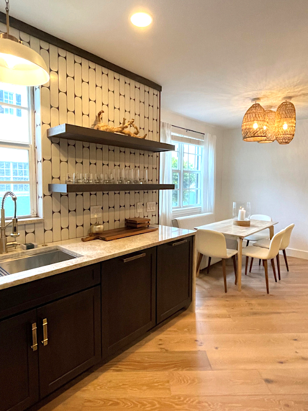 Dark brown shaker base cabinets on the sink wall of a kitchen design with floating wood shelves and a funky white subway tile backsplash