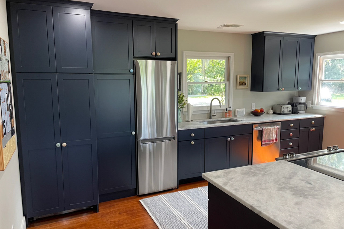 One-wall kitchen remodel with island in navy blue shaker kitchen cabinets with a white and gray quartz countertop and unique map of hilton head on the back of the island