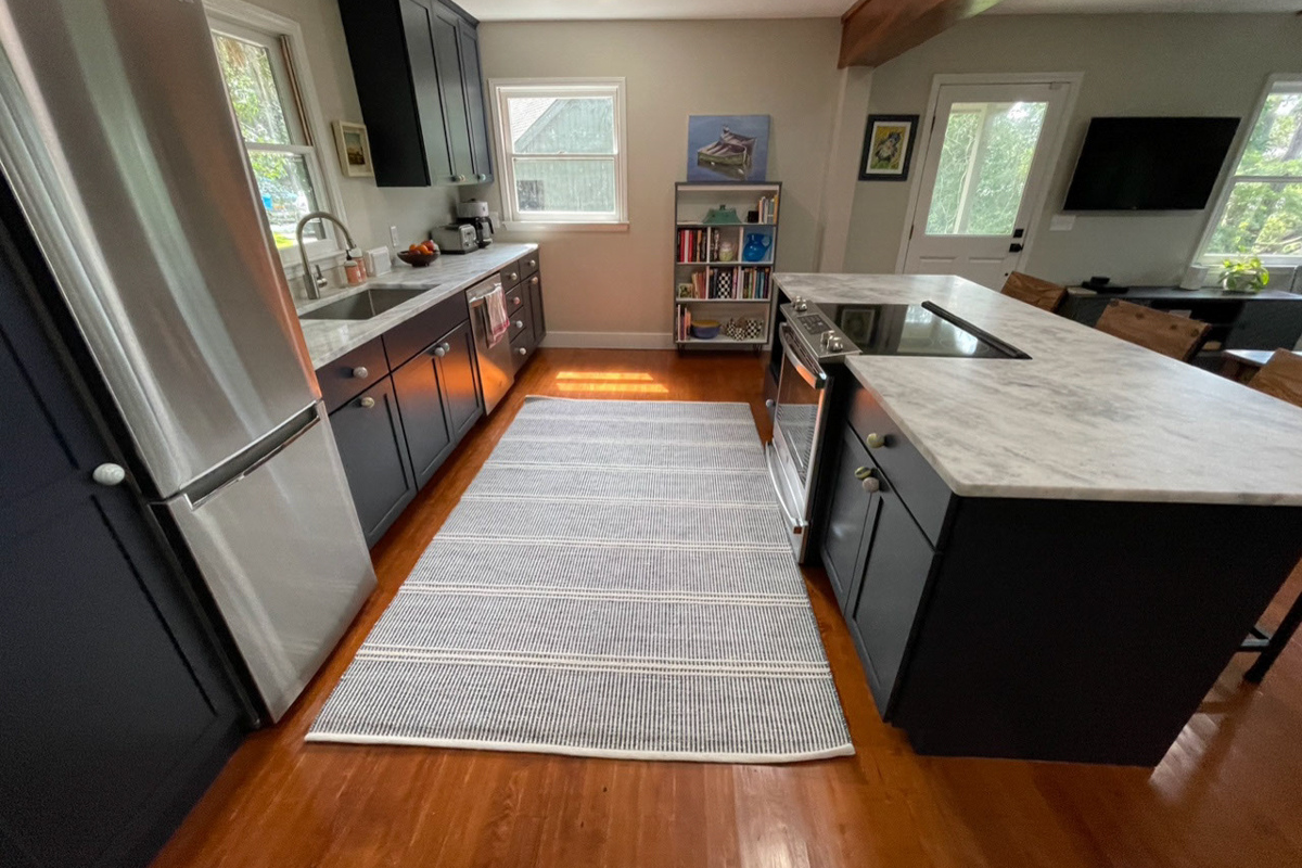 One-wall kitchen remodel with island in navy blue shaker kitchen cabinets with a white and gray quartz countertop and unique map of hilton head on the back of the island