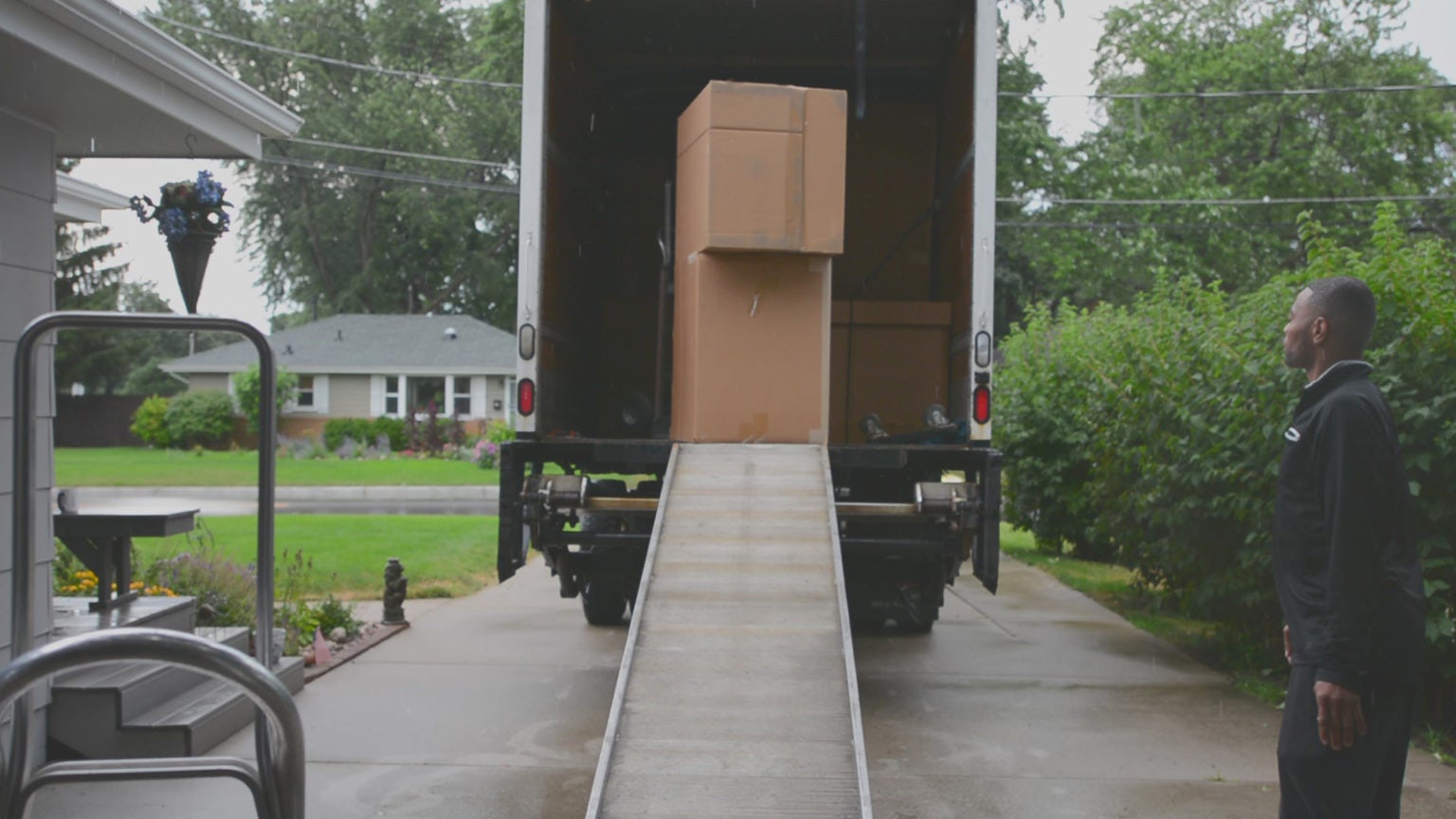 Delivery driver in black clothing waiting at end of trucks ramp for assistant to wheel down cabinet boxes