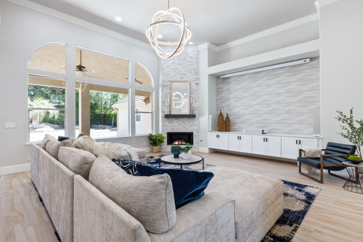 Large living room in neutral and white colors with tall ceilings and white shaker entertainment center cabinets under a large projector screen