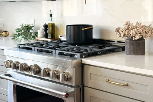 Close-up of a stunning gas chef’s range next to beige kitchen cabinets with shaker door style and brass cabinet hardware 