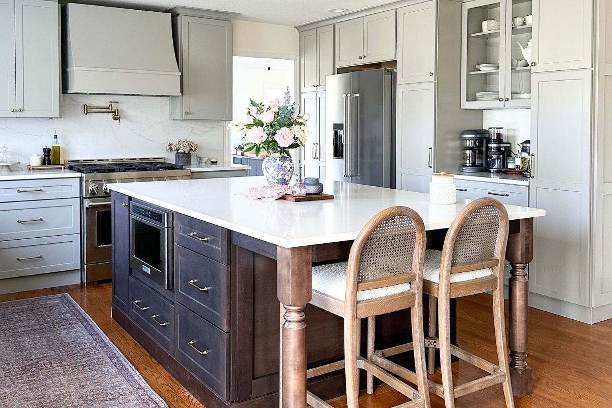 Light gray shaker kitchen with wood hood, white quartz countertops, and a large dark brown furniture-style island