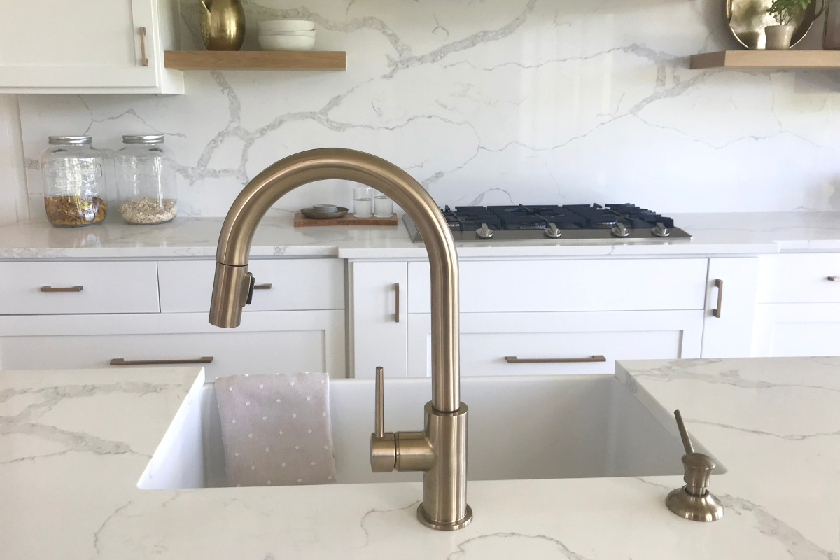 White shaker kitchen cabinets with gold goose neck faucet, cabinet hardware, and decor