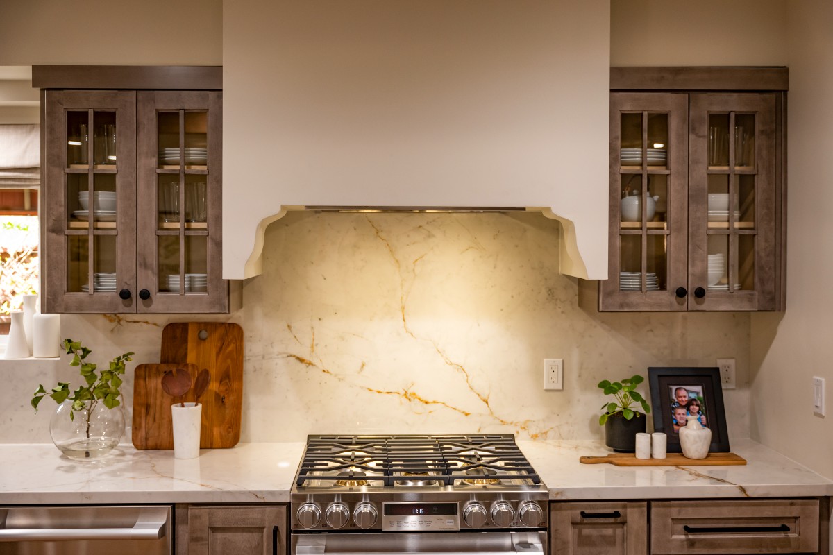 CliqStudios project: Light gray-brown stained kitchen cabinets with mullion doors, cream countertops, and a slab backsplash