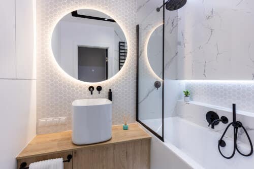 Floating wood vanity with circular mirror with backlighting above