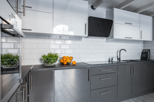 High-gloss kitchen cabinet design with white wall cabinets and gray base cabinets, dark gray countertops and a white subway tile backsplash 