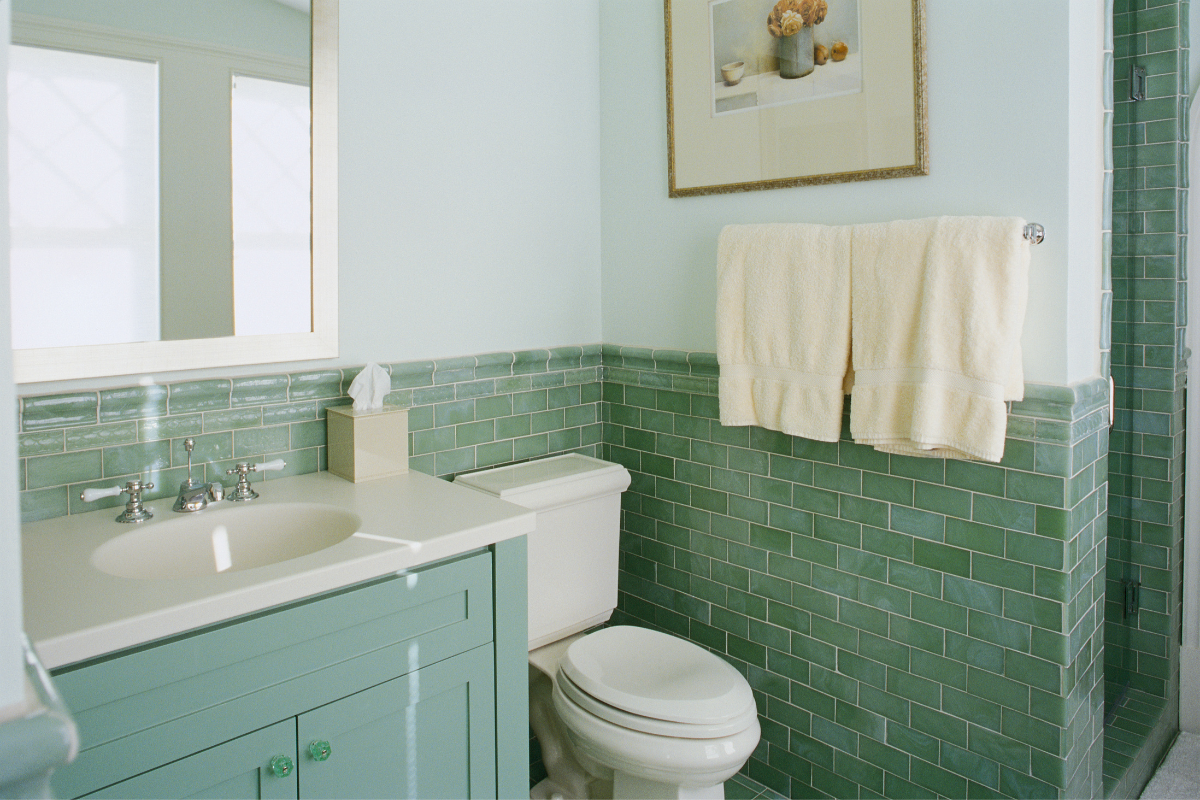 Green bathroom vanity and white countertops surrounded by darker green subway tile