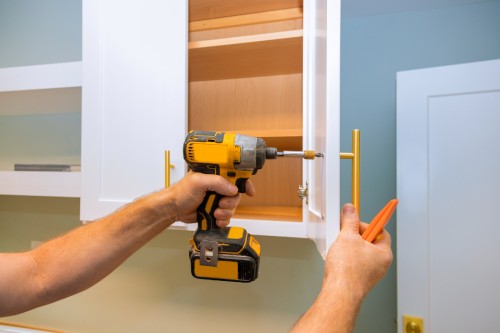 Person installing gold cabinet hardware on white shaker cabinet